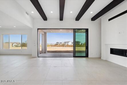 unfurnished living room with recessed lighting, plenty of natural light, beam ceiling, and a glass covered fireplace