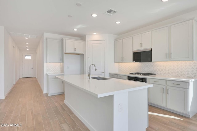 kitchen with stainless steel gas cooktop, sink, white cabinetry, tasteful backsplash, and an island with sink