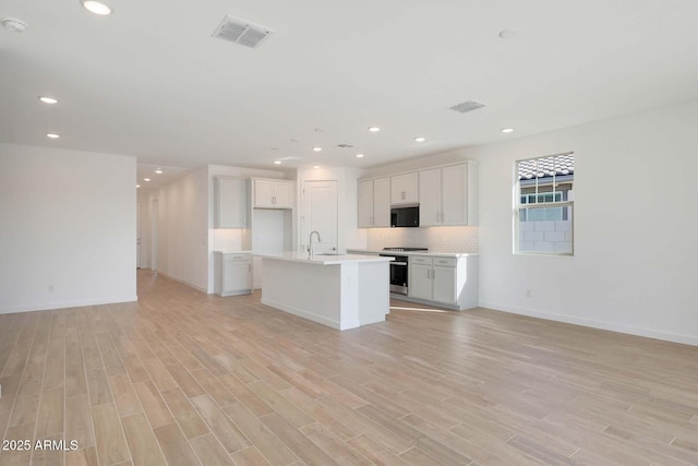 kitchen with decorative backsplash, light hardwood / wood-style flooring, an island with sink, and white cabinets