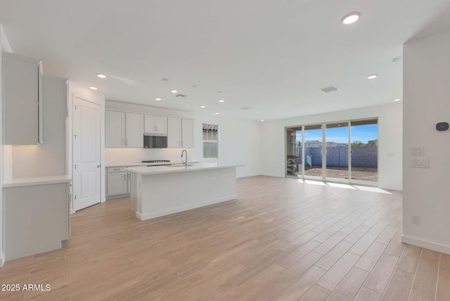 kitchen featuring tasteful backsplash, sink, light hardwood / wood-style flooring, and an island with sink