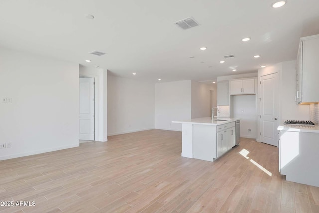 kitchen with dishwasher, an island with sink, sink, white cabinets, and light hardwood / wood-style flooring