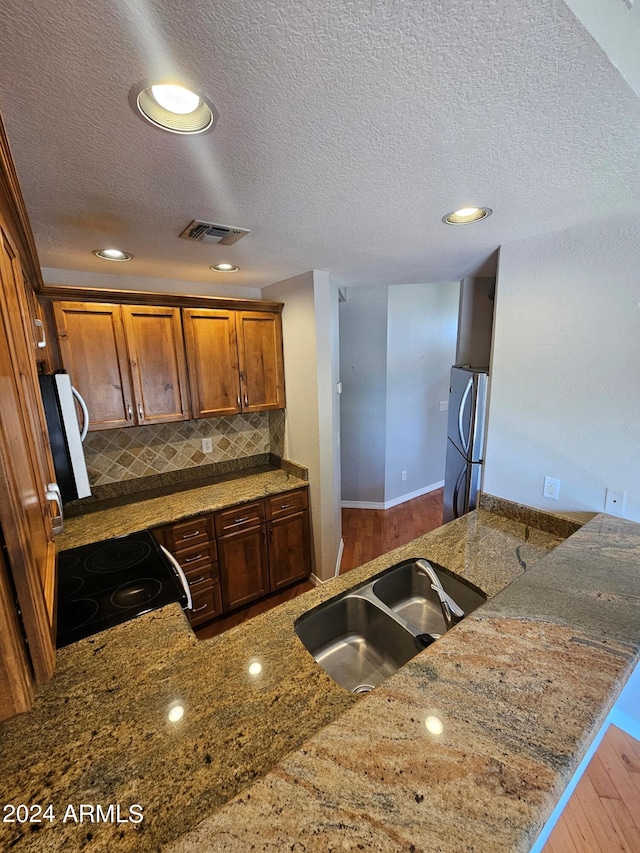 kitchen with sink, electric range, stainless steel refrigerator, kitchen peninsula, and stone counters