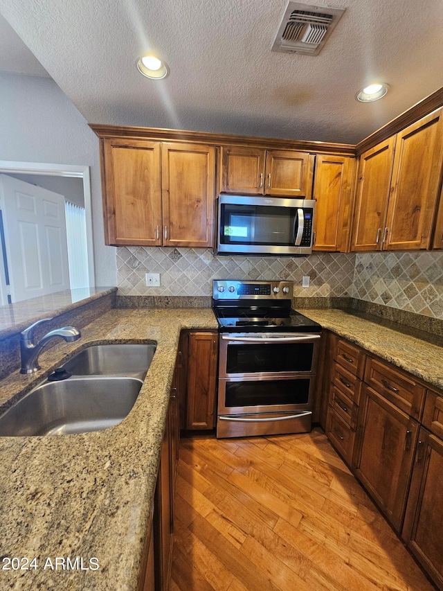 kitchen featuring sink, appliances with stainless steel finishes, light stone counters, decorative backsplash, and light wood-type flooring