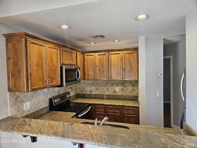 kitchen with appliances with stainless steel finishes, sink, a kitchen breakfast bar, light stone counters, and kitchen peninsula