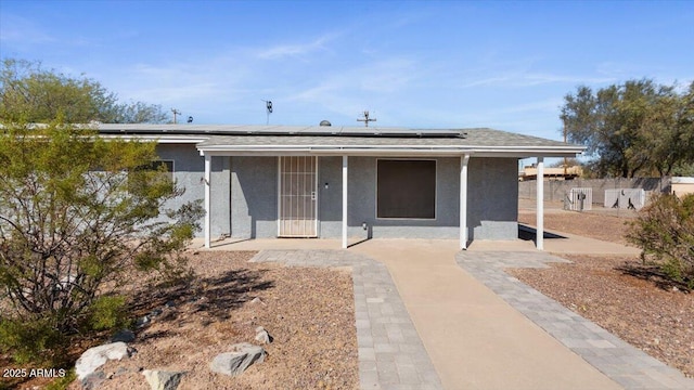 view of front of property with fence, solar panels, and stucco siding