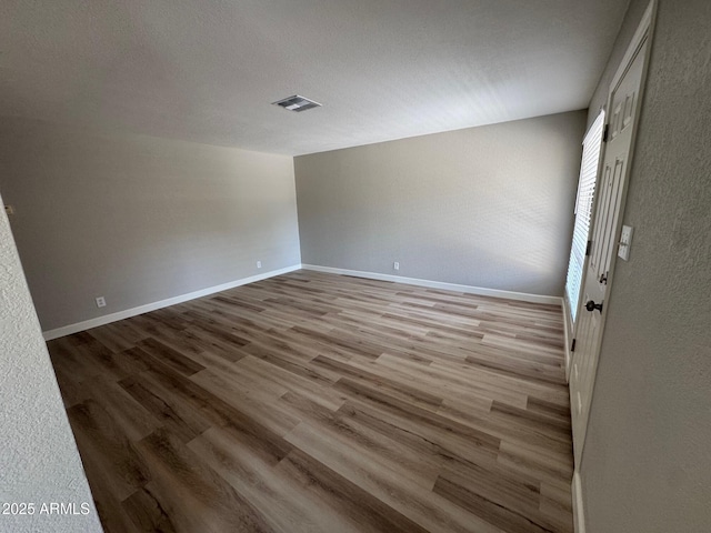 empty room with baseboards, visible vents, a textured wall, and wood finished floors