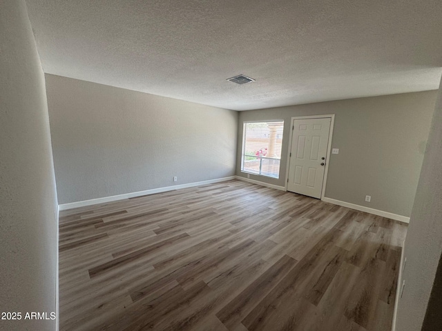 unfurnished room featuring a textured ceiling, baseboards, visible vents, and light wood finished floors