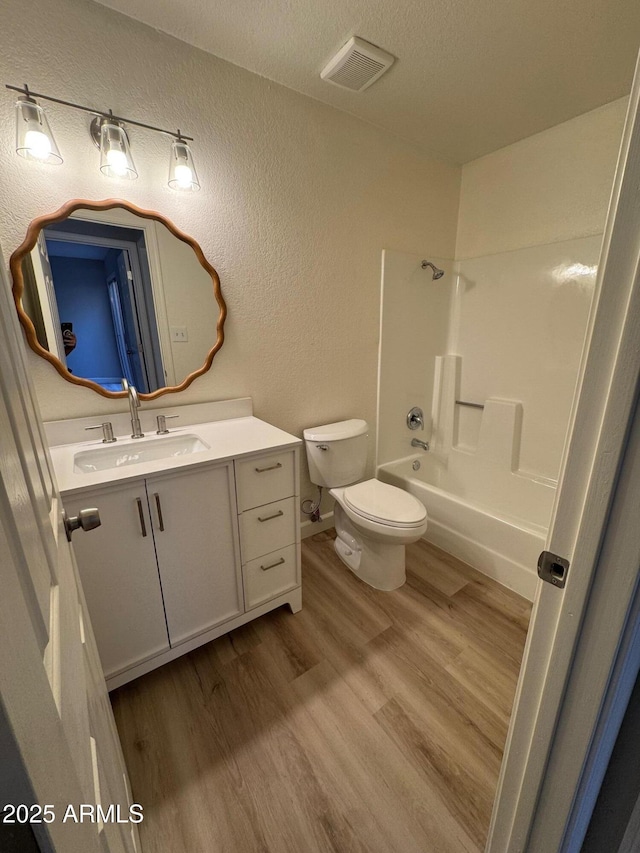 full bath with visible vents, vanity, a textured wall, wood finished floors, and toilet