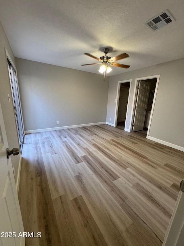 unfurnished bedroom with visible vents, baseboards, a textured ceiling, a ceiling fan, and light wood finished floors