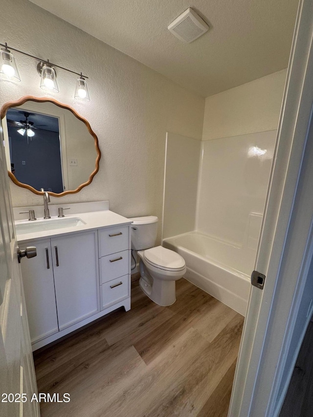 full bath with visible vents, wood finished floors, vanity, toilet, and a textured wall