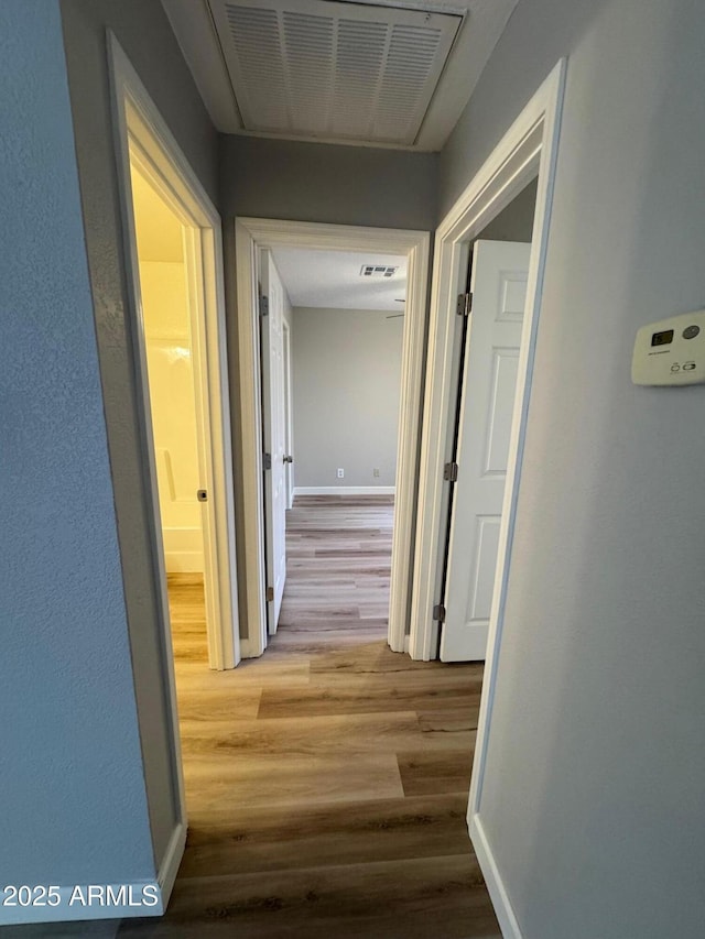 hall featuring baseboards, visible vents, and wood finished floors