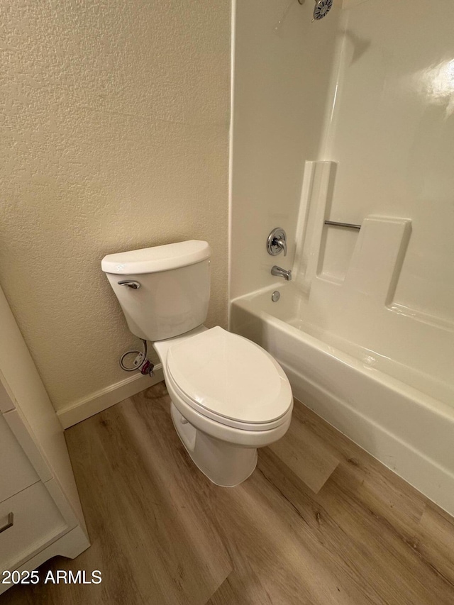 full bathroom with a textured wall, toilet, baseboards, tub / shower combination, and wood finished floors
