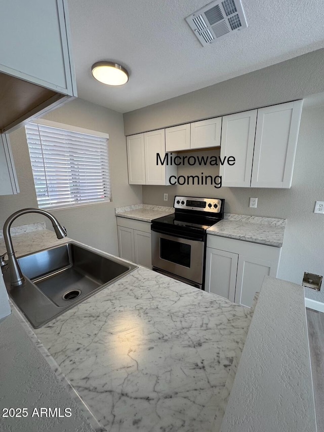 kitchen featuring visible vents, a textured ceiling, white cabinets, stainless steel electric stove, and a sink