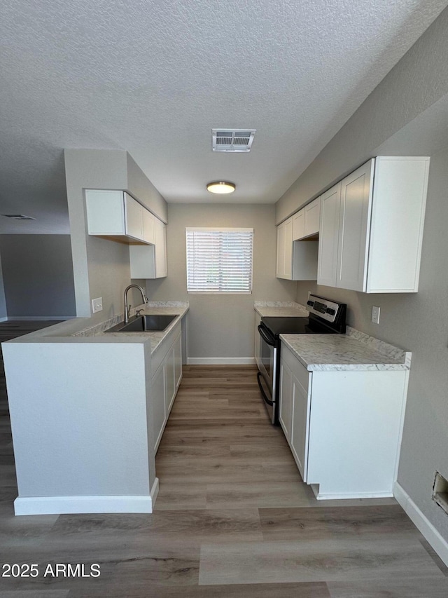 kitchen featuring a sink, stainless steel range with electric stovetop, a textured ceiling, baseboards, and visible vents