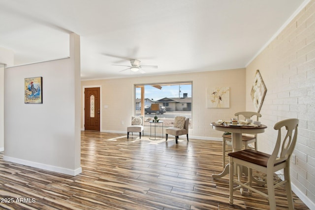 living area with brick wall, ceiling fan, baseboards, and wood finished floors