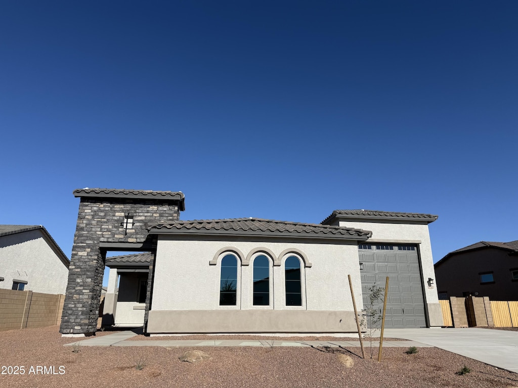 view of front of house featuring a garage, fence, a tile roof, stone siding, and stucco siding