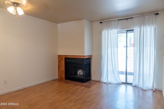 unfurnished living room featuring wood-type flooring, a multi sided fireplace, and ceiling fan