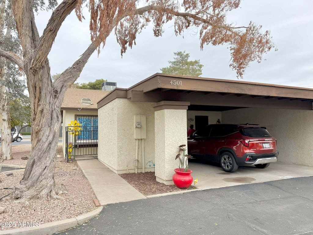 exterior space with stucco siding, a carport, driveway, and a gate