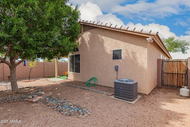 view of side of property featuring a gate, cooling unit, a fenced backyard, and stucco siding