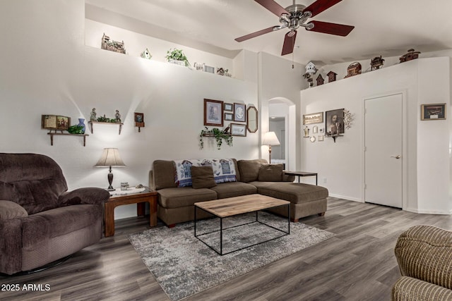 living area with wood finished floors, a ceiling fan, arched walkways, and a towering ceiling