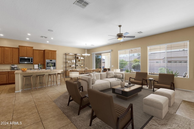 tiled living room with ceiling fan with notable chandelier