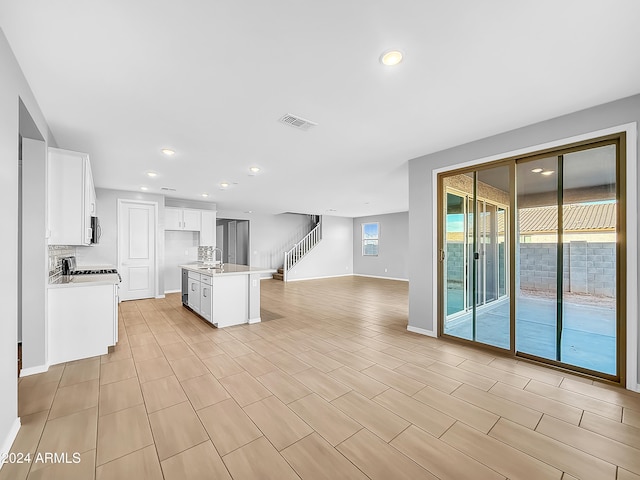 kitchen with sink, an island with sink, decorative backsplash, white cabinets, and light wood-type flooring