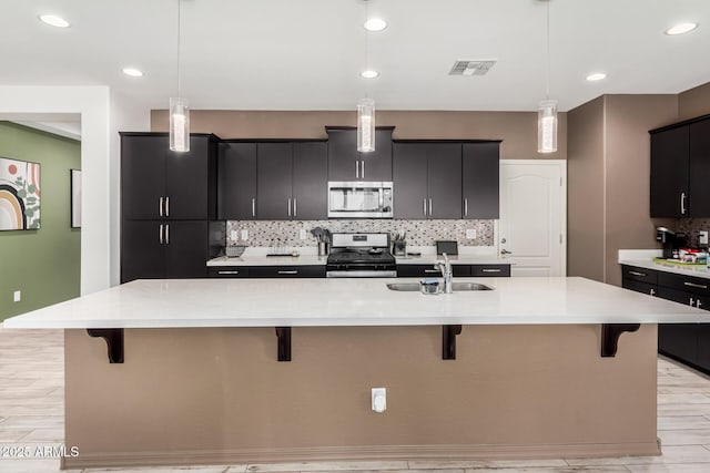 kitchen with visible vents, a breakfast bar, dark cabinets, stainless steel appliances, and a sink