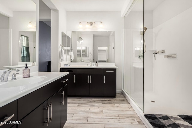 full bath with wood finish floors, a stall shower, two vanities, and a sink