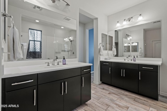 bathroom with a stall shower, two vanities, a sink, and visible vents