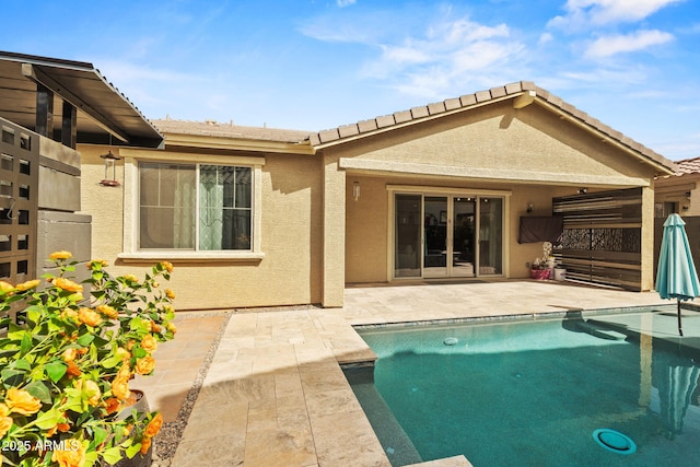 rear view of property with a tile roof, a patio area, an outdoor pool, and stucco siding