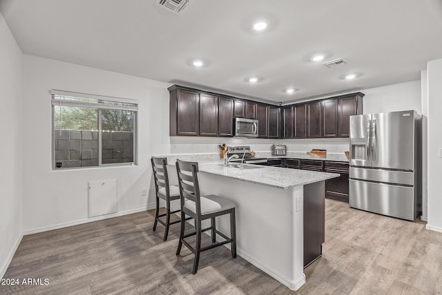 kitchen featuring light stone counters, dark brown cabinetry, stainless steel appliances, sink, and light hardwood / wood-style floors