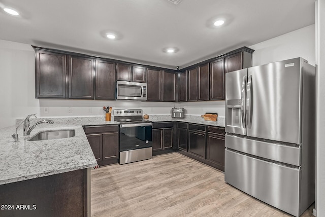 kitchen with sink, light stone countertops, light hardwood / wood-style floors, dark brown cabinetry, and stainless steel appliances