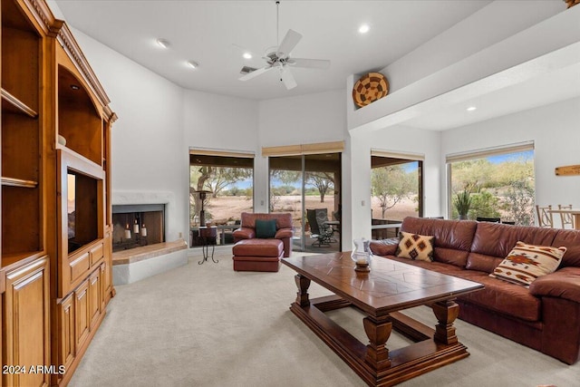 living room featuring a high ceiling, a fireplace, ceiling fan, and light colored carpet