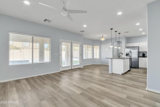 kitchen with ceiling fan, decorative light fixtures, white cabinets, stainless steel fridge with ice dispenser, and an island with sink