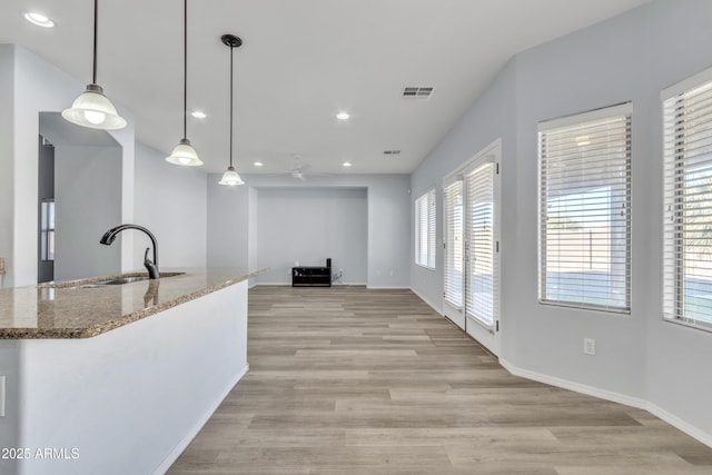 kitchen with light stone countertops, sink, ceiling fan, decorative light fixtures, and light wood-type flooring