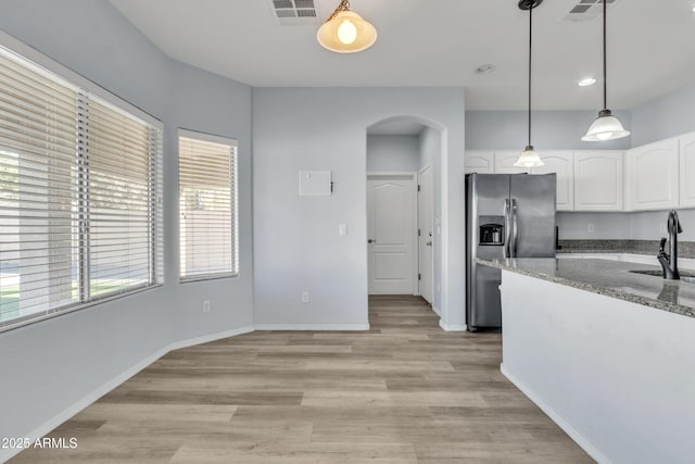 kitchen featuring light stone countertops, a healthy amount of sunlight, stainless steel fridge, decorative light fixtures, and white cabinets