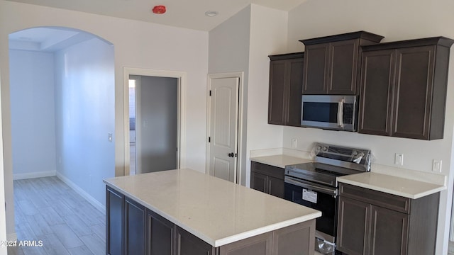 kitchen with dark brown cabinets, a kitchen island, stainless steel appliances, and light hardwood / wood-style floors