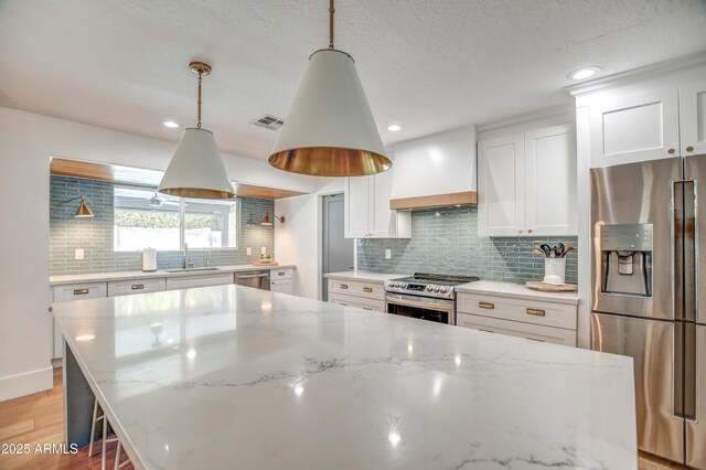 kitchen featuring premium range hood, appliances with stainless steel finishes, pendant lighting, white cabinetry, and light stone counters