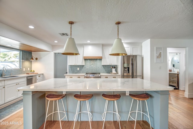 kitchen with premium range hood, a kitchen island, appliances with stainless steel finishes, decorative light fixtures, and light stone countertops