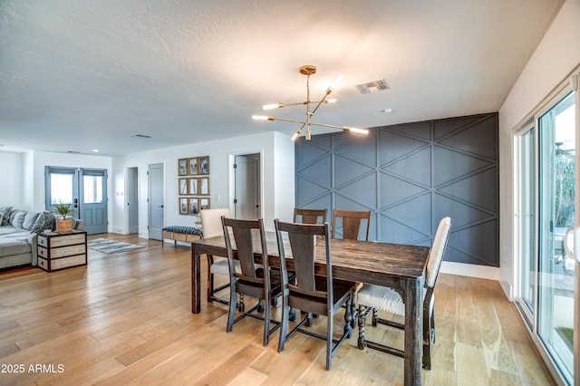 dining area with an inviting chandelier, light hardwood / wood-style flooring, and a textured ceiling