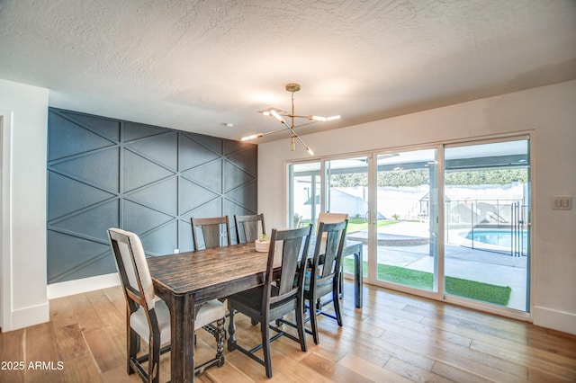 dining area with light hardwood / wood-style floors, a textured ceiling, and a notable chandelier