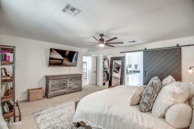 carpeted bedroom with a walk in closet, a barn door, ceiling fan, and a closet