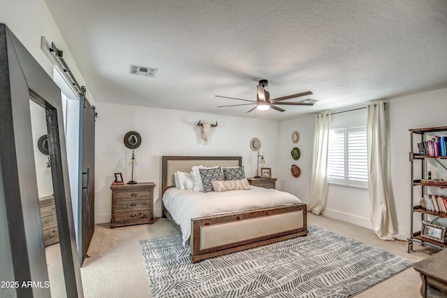 bedroom featuring light carpet, a textured ceiling, a barn door, and ceiling fan