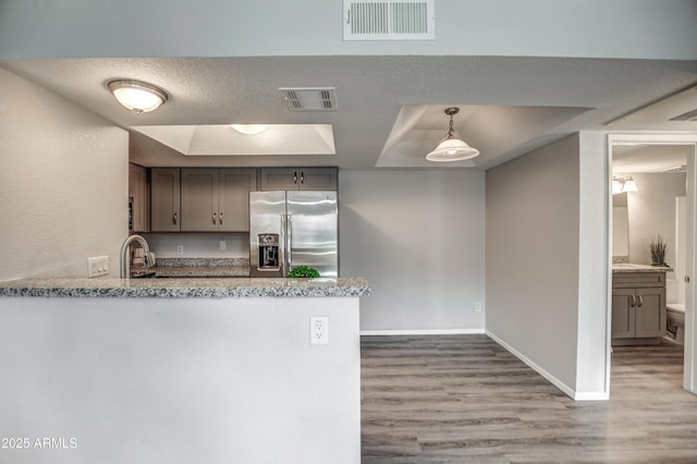 kitchen with stainless steel fridge with ice dispenser, hardwood / wood-style flooring, kitchen peninsula, a raised ceiling, and a textured ceiling