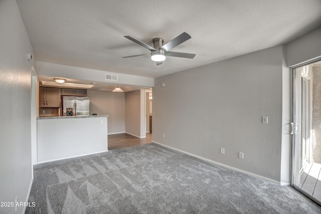 unfurnished living room featuring ceiling fan, dark carpet, and a textured ceiling