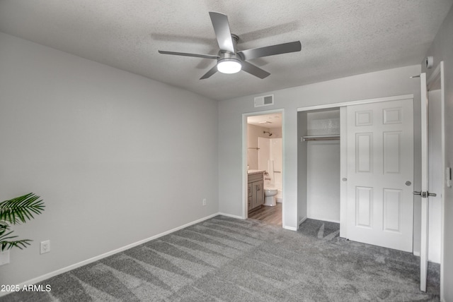 unfurnished bedroom featuring ensuite bath, a textured ceiling, carpet flooring, a closet, and ceiling fan