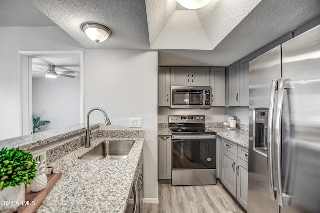 kitchen with sink, light stone counters, a textured ceiling, light wood-type flooring, and appliances with stainless steel finishes