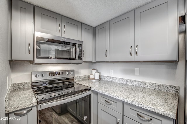 kitchen with appliances with stainless steel finishes, gray cabinetry, hardwood / wood-style floors, light stone countertops, and a textured ceiling