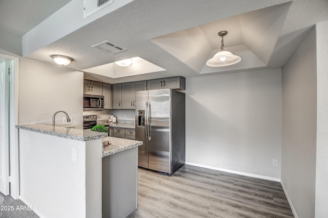 kitchen featuring appliances with stainless steel finishes, hanging light fixtures, light hardwood / wood-style floors, a textured ceiling, and kitchen peninsula