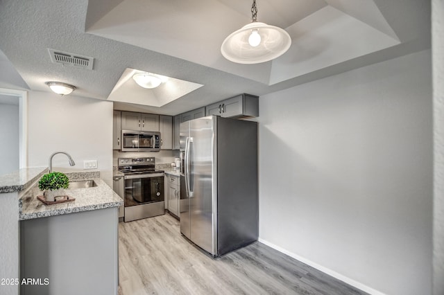 kitchen with pendant lighting, appliances with stainless steel finishes, gray cabinetry, a tray ceiling, and kitchen peninsula